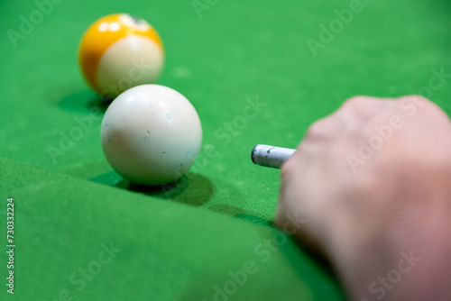 Young adult bearder male playing billiards with his friends focusing on white ball to hit it with muscular hand photo