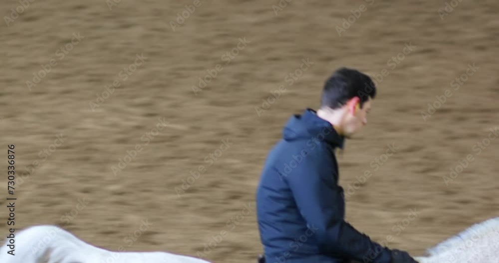 Horseman in black rides white horse in indoor hippodrome with sand Horseman in black rides white horse in indoor hippodrome with sand