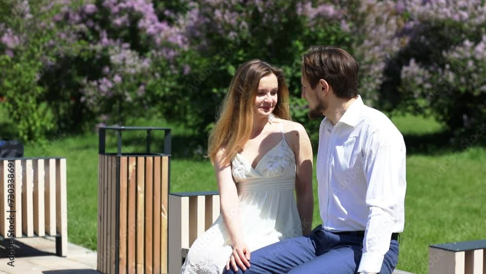 Happy woman and man sits on bench in park with lilac at sunny day, slow motion Happy woman and man sits on bench in park with lilac at sunny day, slow motion