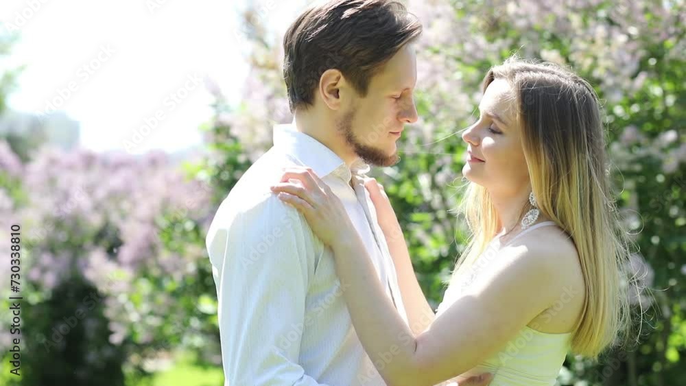 Happy woman and man stand together in park with lilac at sunny day, slow motion Happy woman and man stand together in park with lilac at sunny day, slow motion