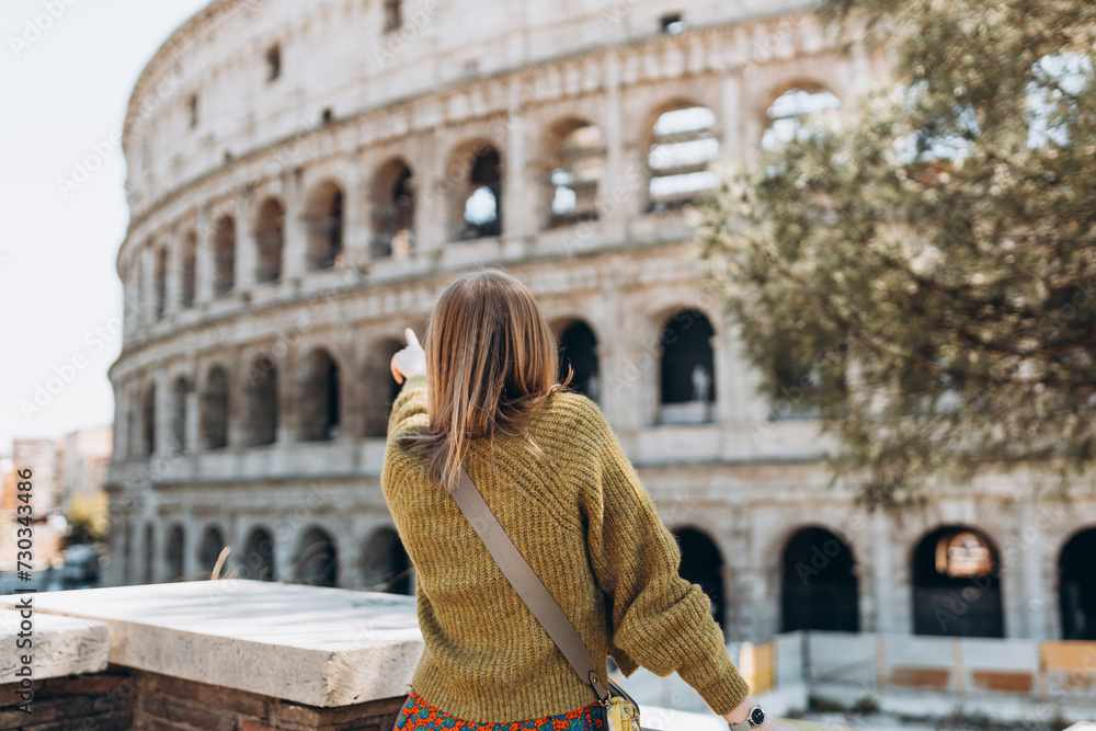 A happy blond woman tourist is standing near the Coliseum, old ruins at the center of Rome, Italy. Concept of traveling famous landmarks. 30s Girl is walking on a sunny day