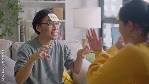 Smiling Asian Couple having fun playing word guessing game at home.asia woman and japanese man playing guessing game sitting on sofa during long weekend holiday.couple playing game,Lifestyle concept