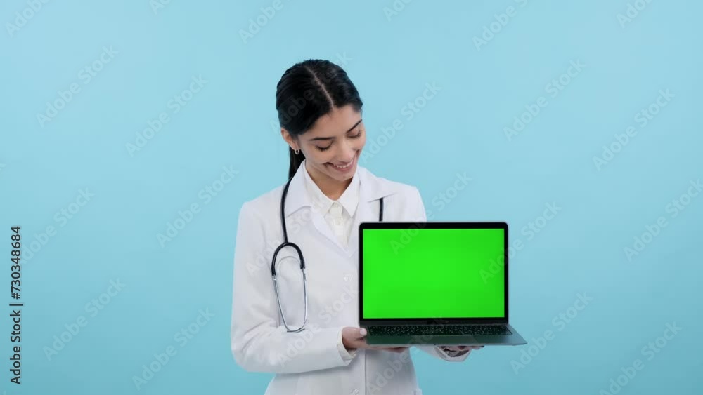 Smiling doctor or nurse in a medical lad coat holds a laptop with a green screen for advertising on a blue background. Device screen, blend of medicine and technology concept. Smiling doctor or nurse in a medical lad coat holds a laptop with a green screen for advertising on a blue background. Device screen, blend of medicine and technology concept.