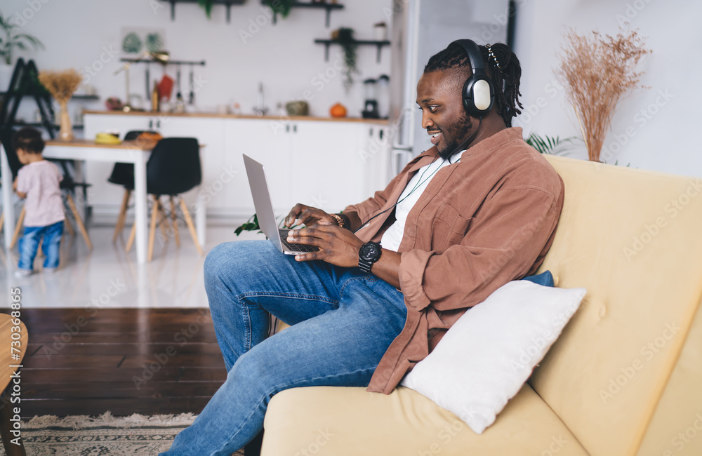 Positive black man in headphones using laptop while working at home