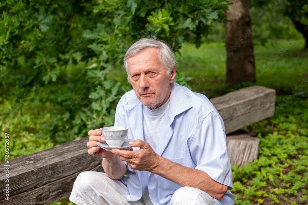 An elderly man sits alone on a wooden bench and looking in camera, holding a cup of coffee. The serene setting conveys a peaceful, contemplative mood, suitable for wellness themes, senior insurance An elderly man sits alone on a wooden bench and looking in camera, holding a cup of coffee. The serene setting conveys a peaceful, contemplative mood, suitable for wellness themes, senior insurance
