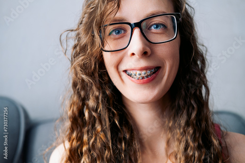 smile of a long-haired young woman in glasses with blue eyes in braces close-up