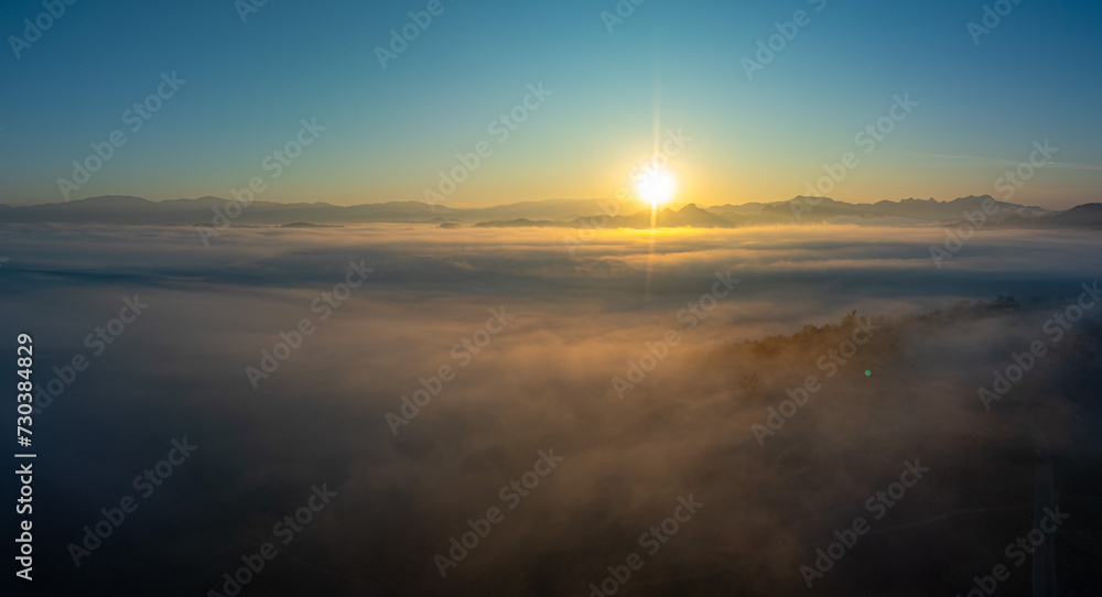 Obraz premium Aerial view amazing the sea of mist at beautiful sunrise...slow floating fog blowing cover on the top of mountain look like as a sea of mist. ..white cloud in blue sky over the perfect forest.