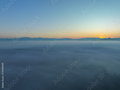 aerial view a sea of white mist envelops the mountain peak, slowly flowing down from the mountain peak...The mist poured down from the mountains in the morning...the sea of mist background. © Narong Niemhom