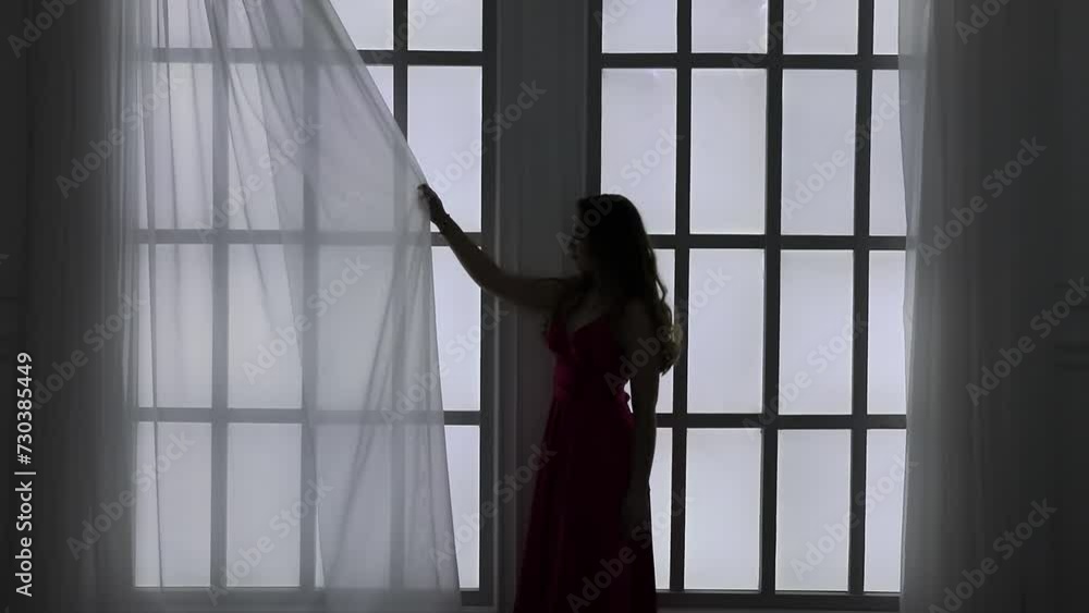 Silhouette of woman which draws curtains on bright window Silhouette of woman which draws curtains on bright window