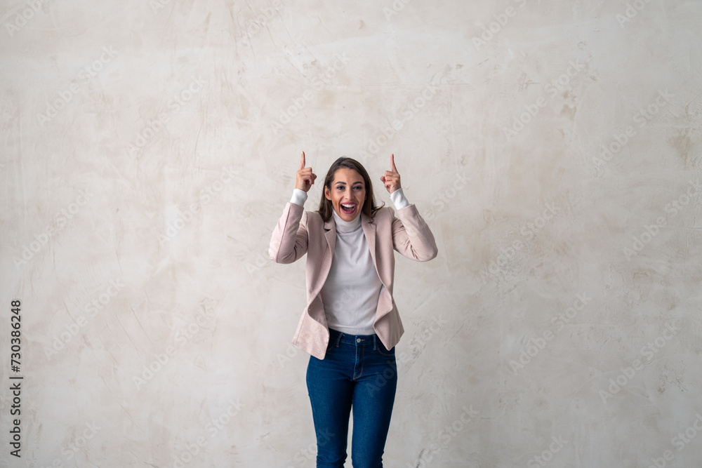 Attractive excited woman pointing up in studio for announcement, info or promo. Adult female and smile for business, showing deal or discount with hand and joy on copy space. Attractive excited woman pointing up in studio for announcement, info or promo. Adult female and smile for business, showing deal or discount with hand and joy on copy space.