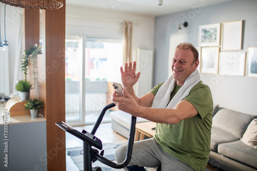 Middle aged man using smartphone on home exercise bike photo