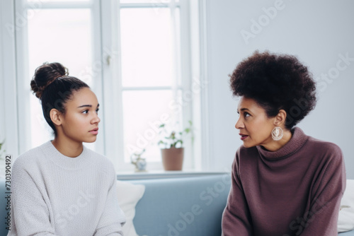 Two women on a couch, engrossed in a heartfelt conversation. The young woman looks worried while the other listens attentively, offering support
