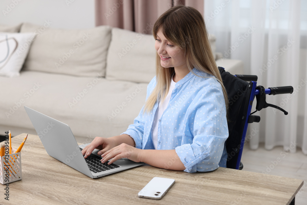 Woman in wheelchair using laptop at table in home office Woman in wheelchair using laptop at table in home office