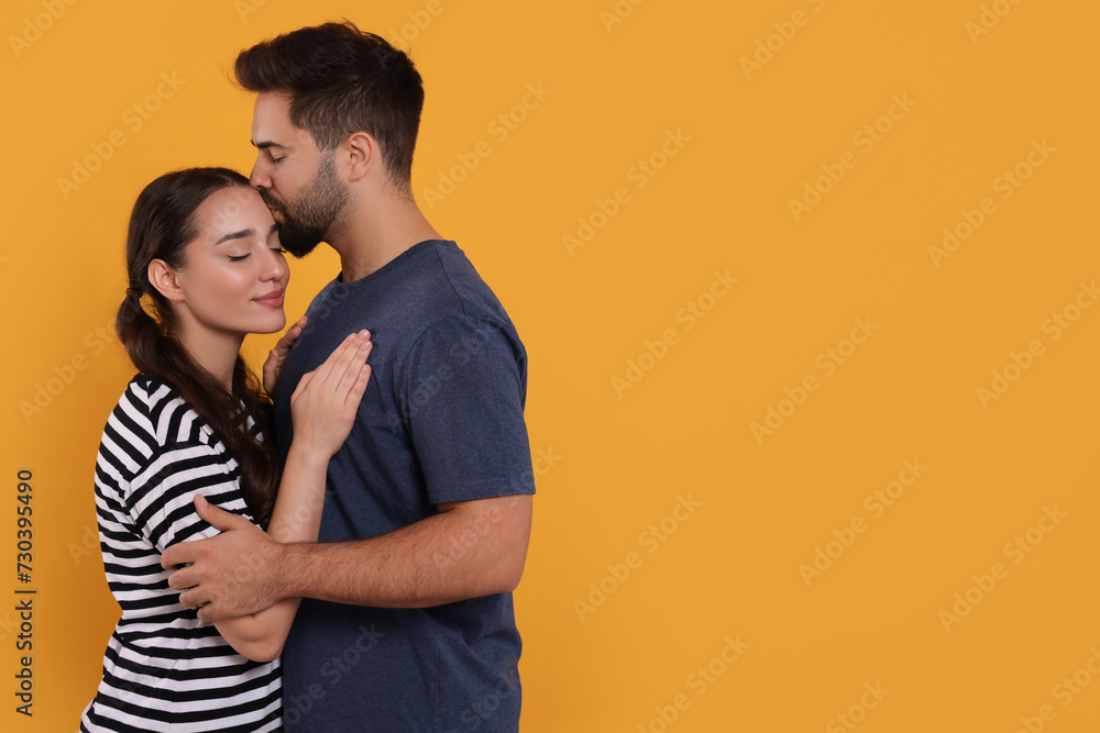 Man kissing his girlfriend on orange background. Space for text Man kissing his girlfriend on orange background. Space for text
