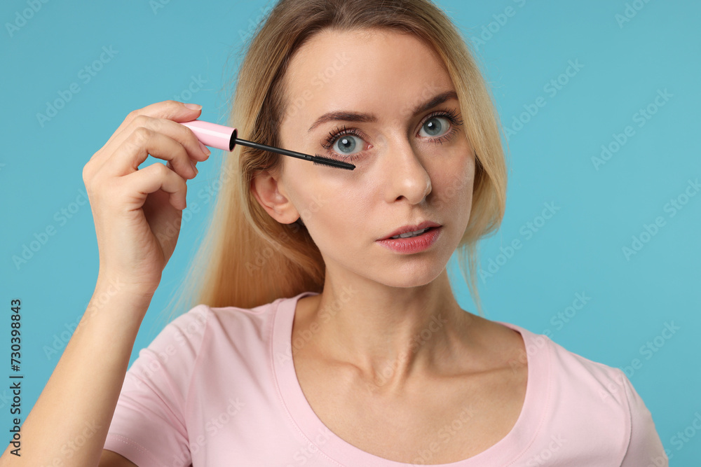 Beautiful woman applying mascara on light blue background, closeup Beautiful woman applying mascara on light blue background, closeup