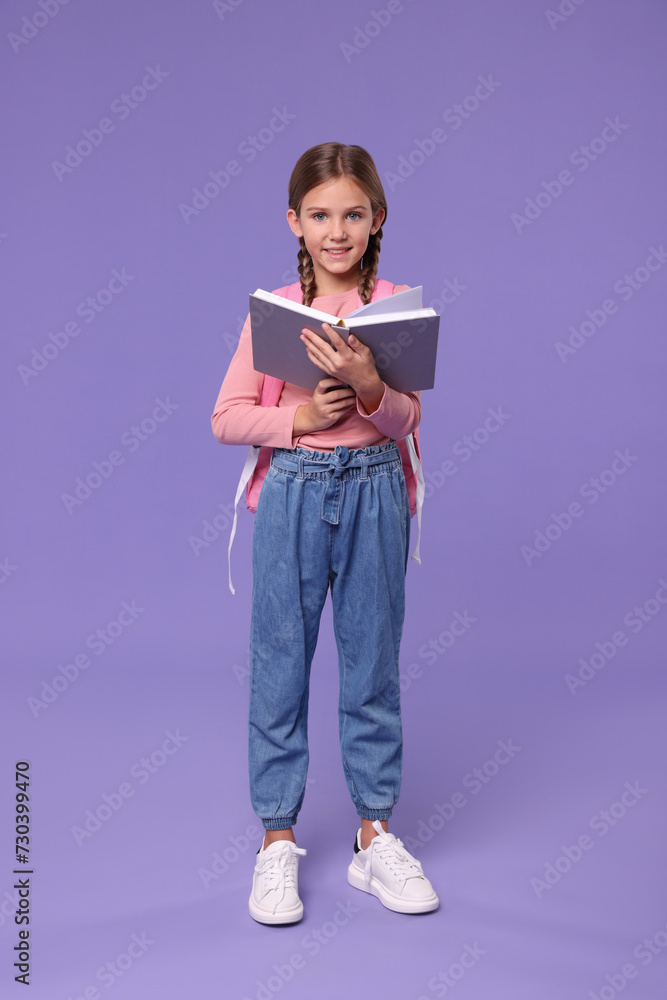 Smiling schoolgirl with open book on violet background Smiling schoolgirl with open book on violet background