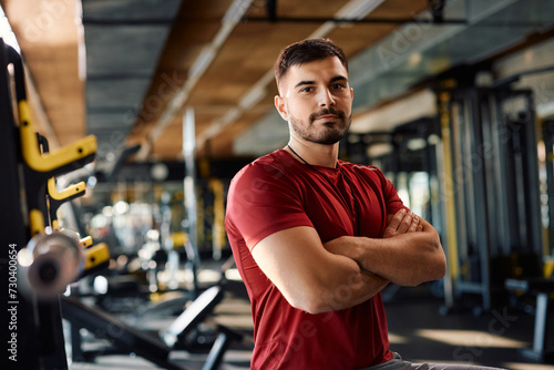 Confident personal trainer with arms crossed in gym looking at camera.