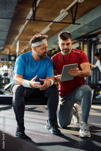 Personal trainer and mature man using digital tablet during gym workout.
