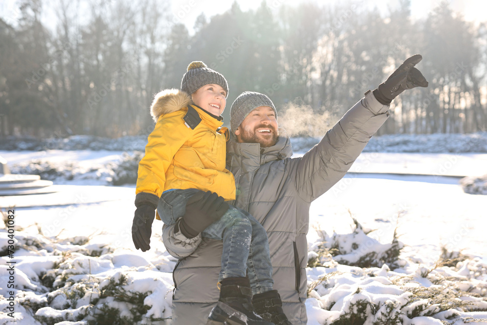 Happy father pointing at something to his son in sunny snowy park