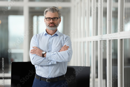 Handsome man with crossed arms in office, space for text. Lawyer, businessman, accountant or manager