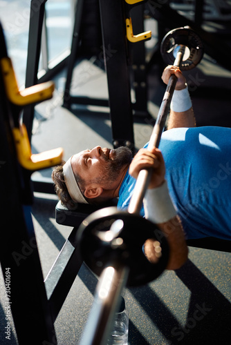 Mature athlete exercising with barbell during his sports training in gym.