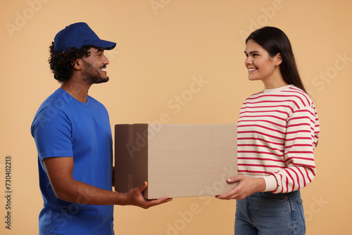 Smiling courier giving parcel to receiver on light brown background