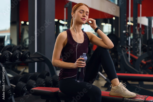 Athletic young woman with earphones and bottle of water in gym
