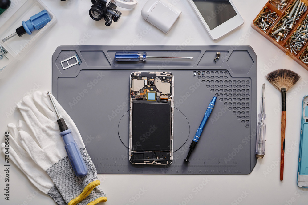 Flat lay shot of parts of disassembled cell phone and work tools displayed on table before repairing