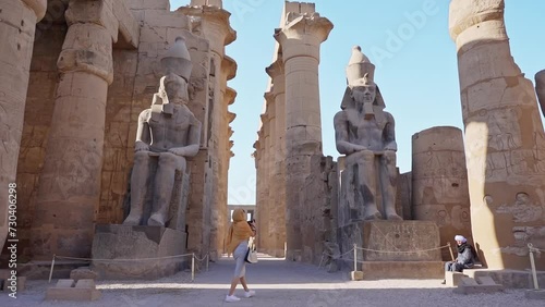 beautiful tourist holding a camera taking pictures of ramsses statue and her family in luxor temple, Luxor, Egypt. photo