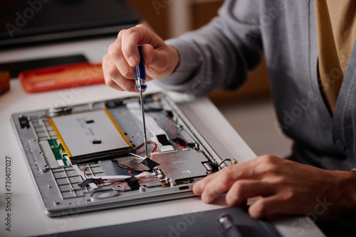 Unrecognizable engineer using screwdriver repairing element of disassembled laptop