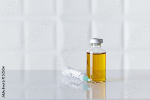 Glass bottle of injectable medicine and a syringe on white medical or pharmaceutical laboratory table. Textured white background.