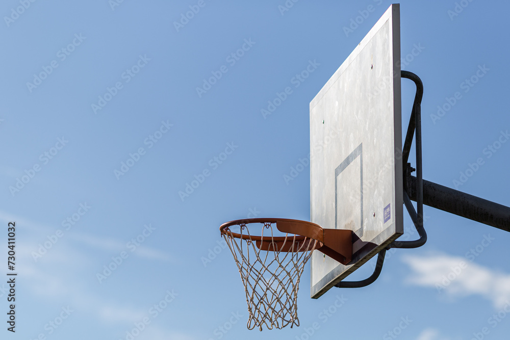 A basketball hoop and backboard outdoors with blue sky and net