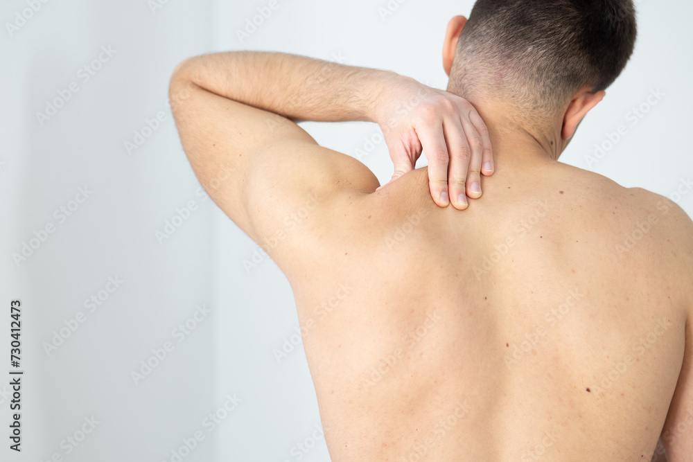 Rear view of a shirtless young man holding his neck in pain isolated on white background, man giving himself a massage on his neck, shirtless man touching his neck, stress, neck pain, upper back pain Rear view of a shirtless young man holding his neck in pain isolated on white background, man giving himself a massage on his neck, shirtless man touching his neck, stress, neck pain, upper back pain