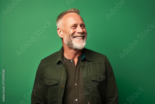 Portrait of a smiling senior man on a green studio background. © Iigo