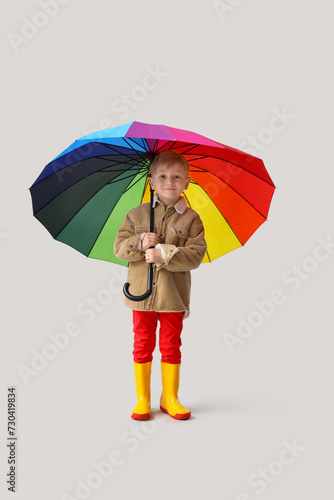 Little boy in rubber boots with umbrella on light background