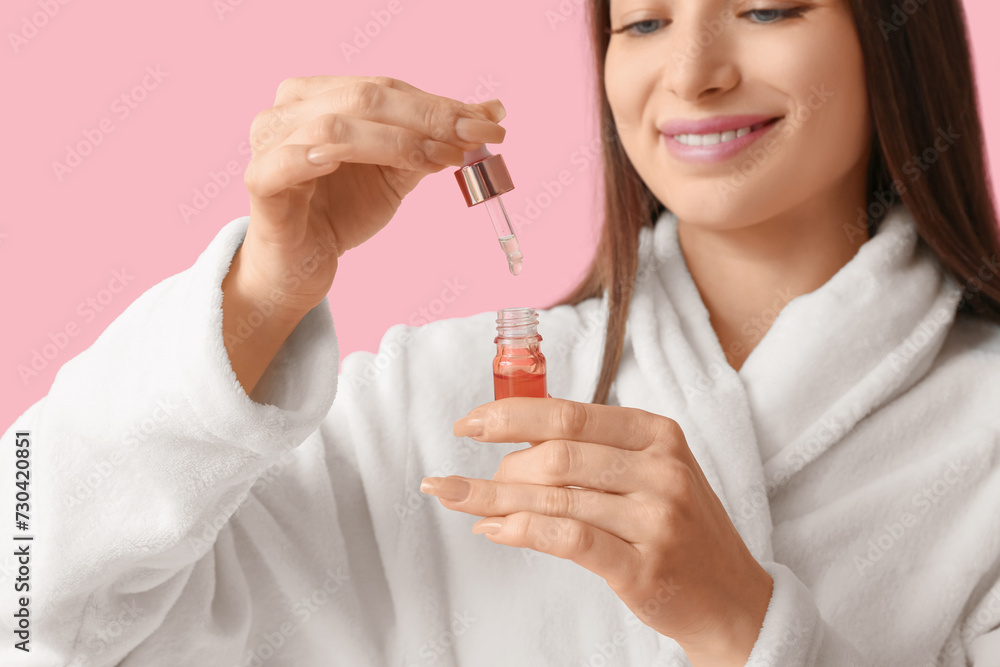 Beautiful woman in bathrobe with serum on pink background, closeup Beautiful woman in bathrobe with serum on pink background, closeup