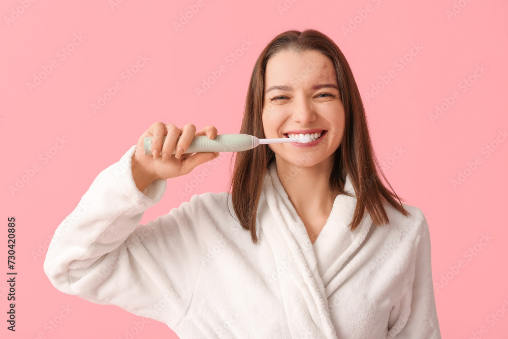 Beautiful woman in bathrobe with electric toothbrush on pink background Beautiful woman in bathrobe with electric toothbrush on pink background