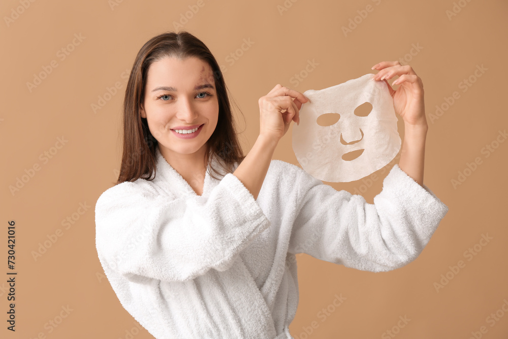 Beautiful woman in bathrobe with facial sheet mask on beige background Beautiful woman in bathrobe with facial sheet mask on beige background