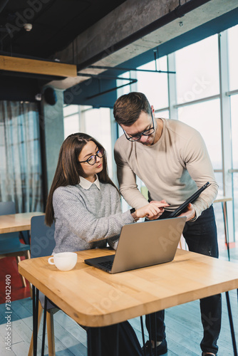 Colleagues communicate while working with a laptop in the office. Two workers in a modern workspace. Two young businessmen are sitting together at a table.