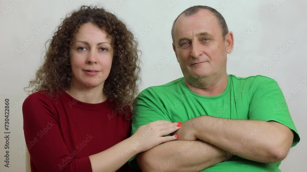 Adult woman with curly hairs puts hand on arm of aged man which sits near, at white background Adult woman with curly hairs puts hand on arm of aged man which sits near, at white background