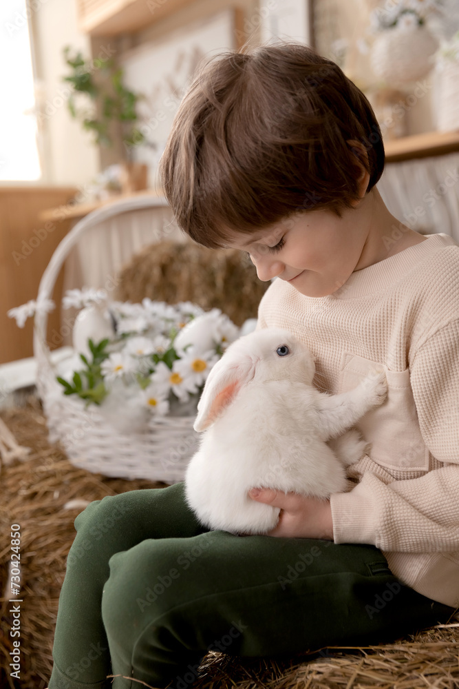 White Easter rabbit sits on the hands of a little boy, who huggs the rabbit White Easter rabbit sits on the hands of a little boy, who huggs the rabbit