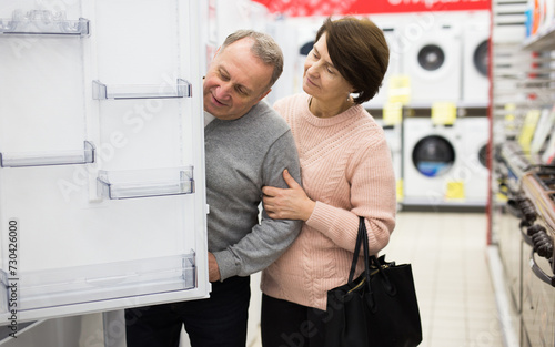 Senior couple choosing refrigerator while shopping in appliance store.