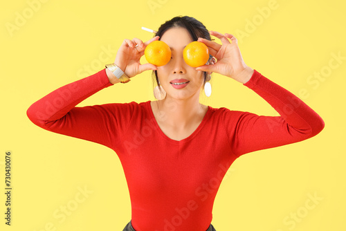 Young Asian woman with mandarins on yellow background. Chinese New Year celebration