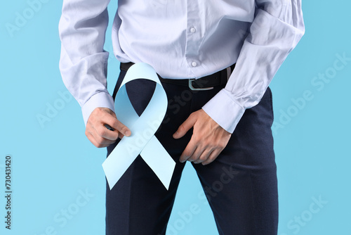 Young businessman with blue ribbon on color background, closeup. Prostate cancer awareness concept