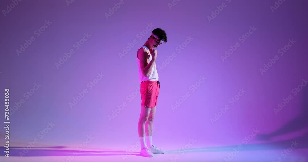 Young Caucasian young 80s man engaged in bicep training with dumbbell, smiling and looking at camera, standing over purple background. Young Caucasian young 80s man engaged in bicep training with dumbbell, smiling and looking at camera, standing over purple background.