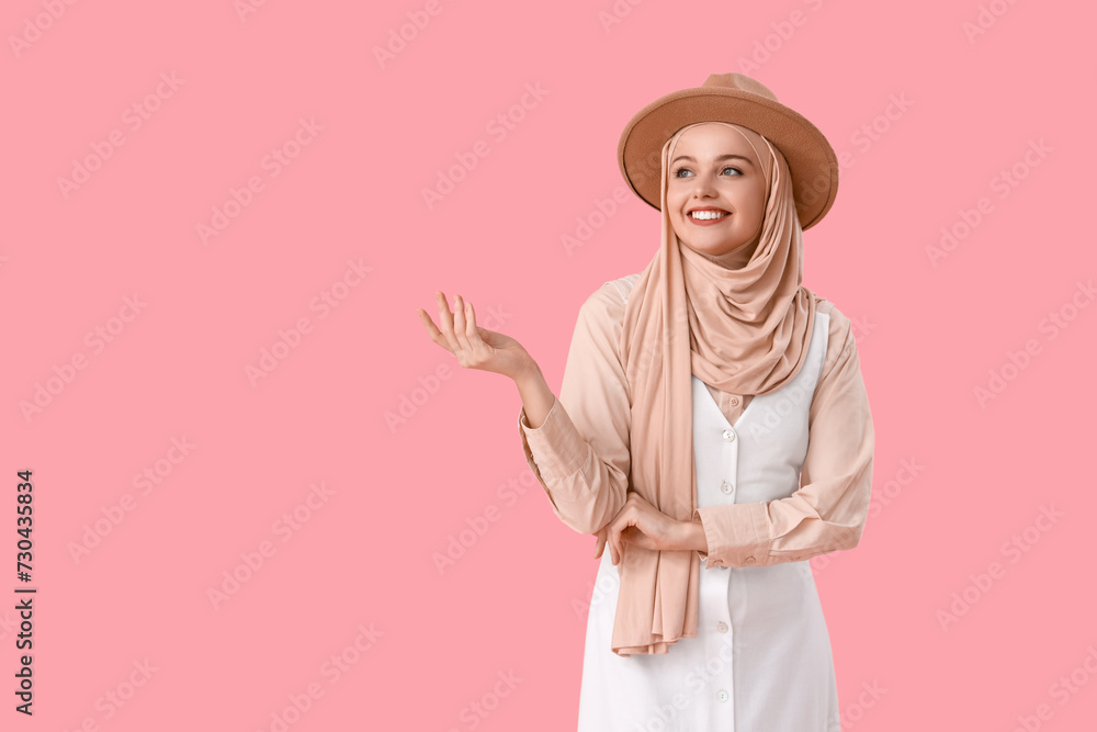 Young Muslim woman in hijab with hat on pink background Young Muslim woman in hijab with hat on pink background