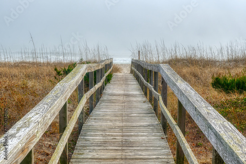 A wooden boardwalk landscape over the grassy sand dunes at a foggy Kure Beach in Wilmington  North Carolina in HDR.