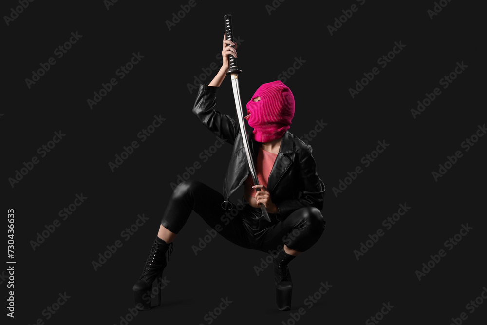 Beautiful young stylish woman in balaclava with sword on black background Beautiful young stylish woman in balaclava with sword on black background