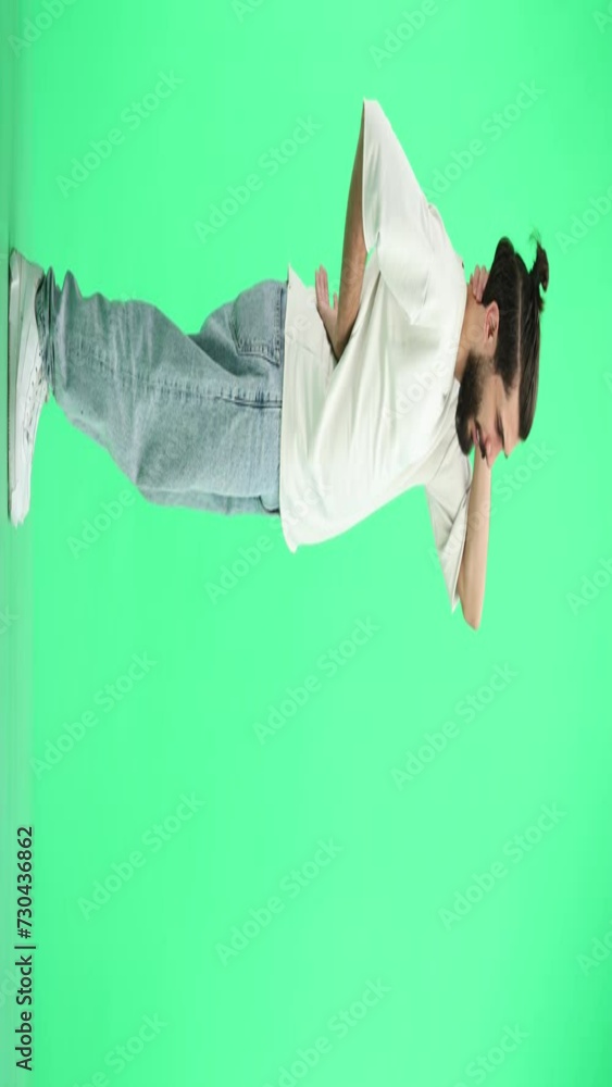 A man, full-length, on a green background, looks into the distance