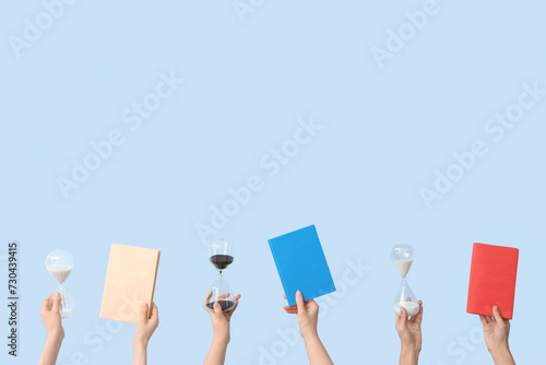 Female hands holding hourglasses and books on blue background